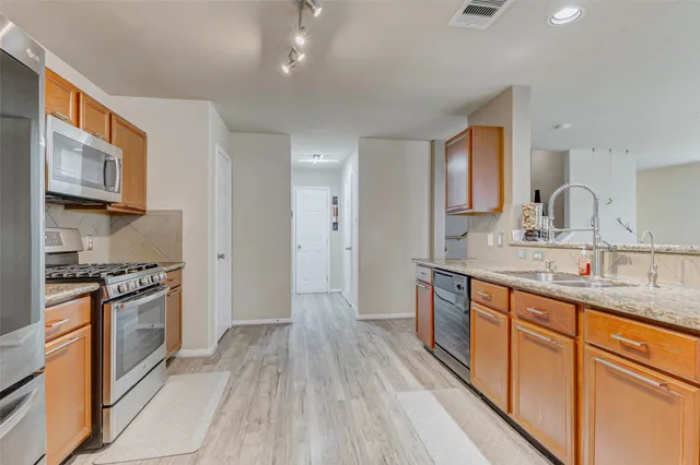 a kitchen with stainless steel appliances granite countertop a stove top oven a sink dishwasher and a refrigerator with wooden floor