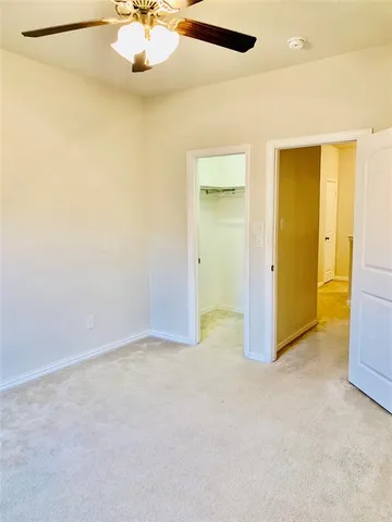 an empty room with a chandelier fan and kitchen view