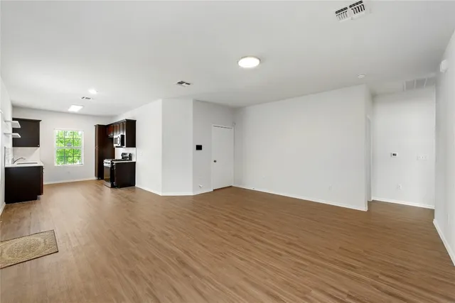 a view of an empty room with wooden floor and a kitchen