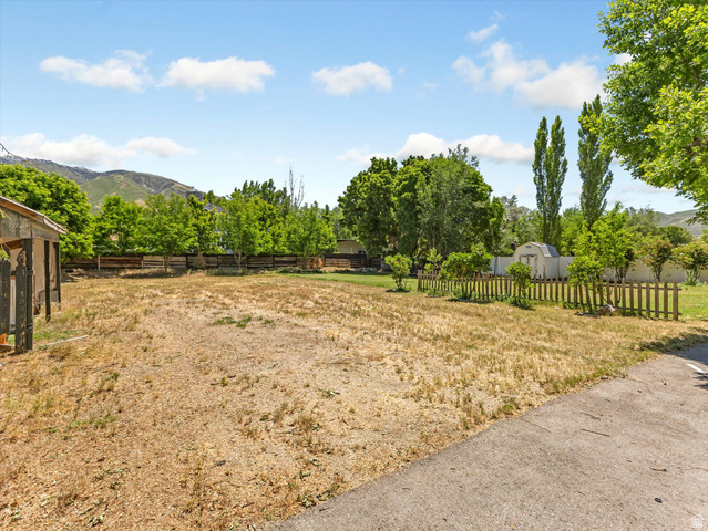 12825 South Fort Street Draper, UT 84020 - Photo 36 of 52 Expansive lot featuring a partial concrete driveway, mature perimeter trees, a wood privacy fence, and a distant mountain backdrop