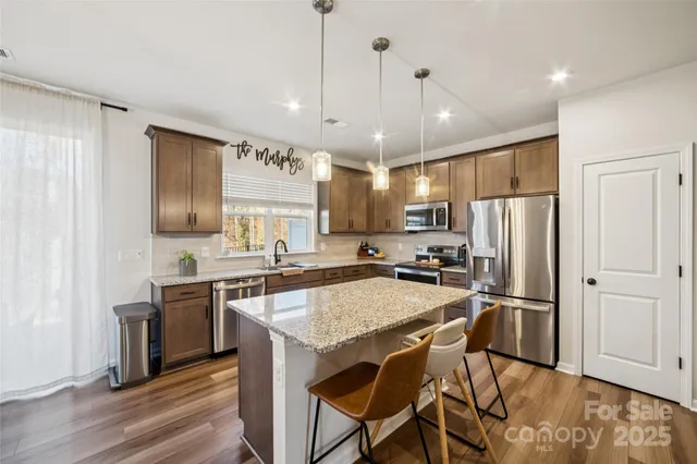 a open kitchen with stainless steel appliances granite countertop a stove a refrigerator a kitchen island a dining table and chairs with wooden floor