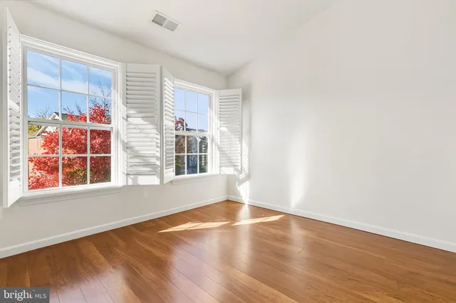 an empty room with wooden floor chandelier fan and windows