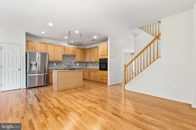 a kitchen with stainless steel appliances granite countertop a refrigerator a sink dishwasher a stove and white cabinets with wooden floor