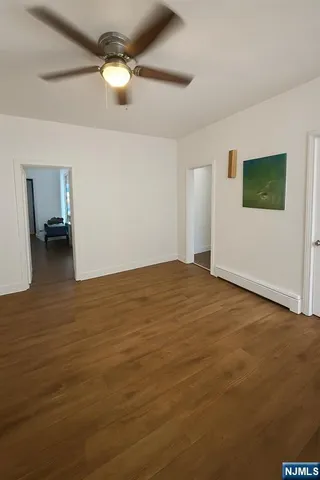 a view of an empty room with chandelier fan and wooden floor