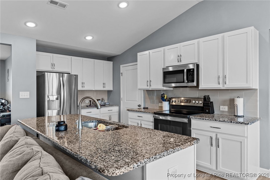 522 Carolina Church Road St. Pauls, NC 28384 - Photo 4 of 36 a kitchen with stainless steel appliances granite countertop a stove top oven a sink a refrigerator and white cabinets