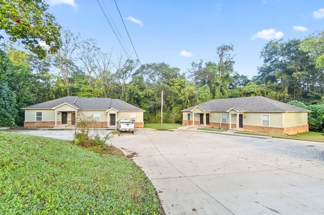 a white house with a big yard plants and large trees