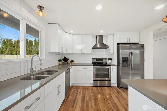 a kitchen with a sink dishwasher a refrigerator and a stove with wooden floor