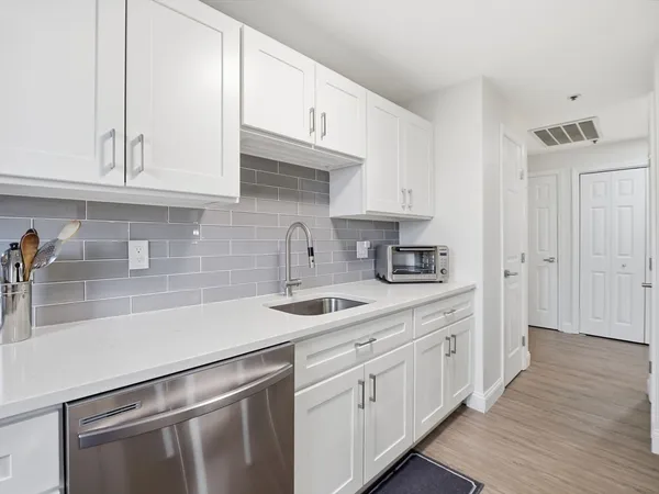a kitchen with stainless steel appliances granite countertop a sink a stove and white cabinets with wooden floor