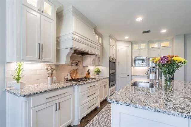 a kitchen with granite countertop a sink a potted plant and white cabinets