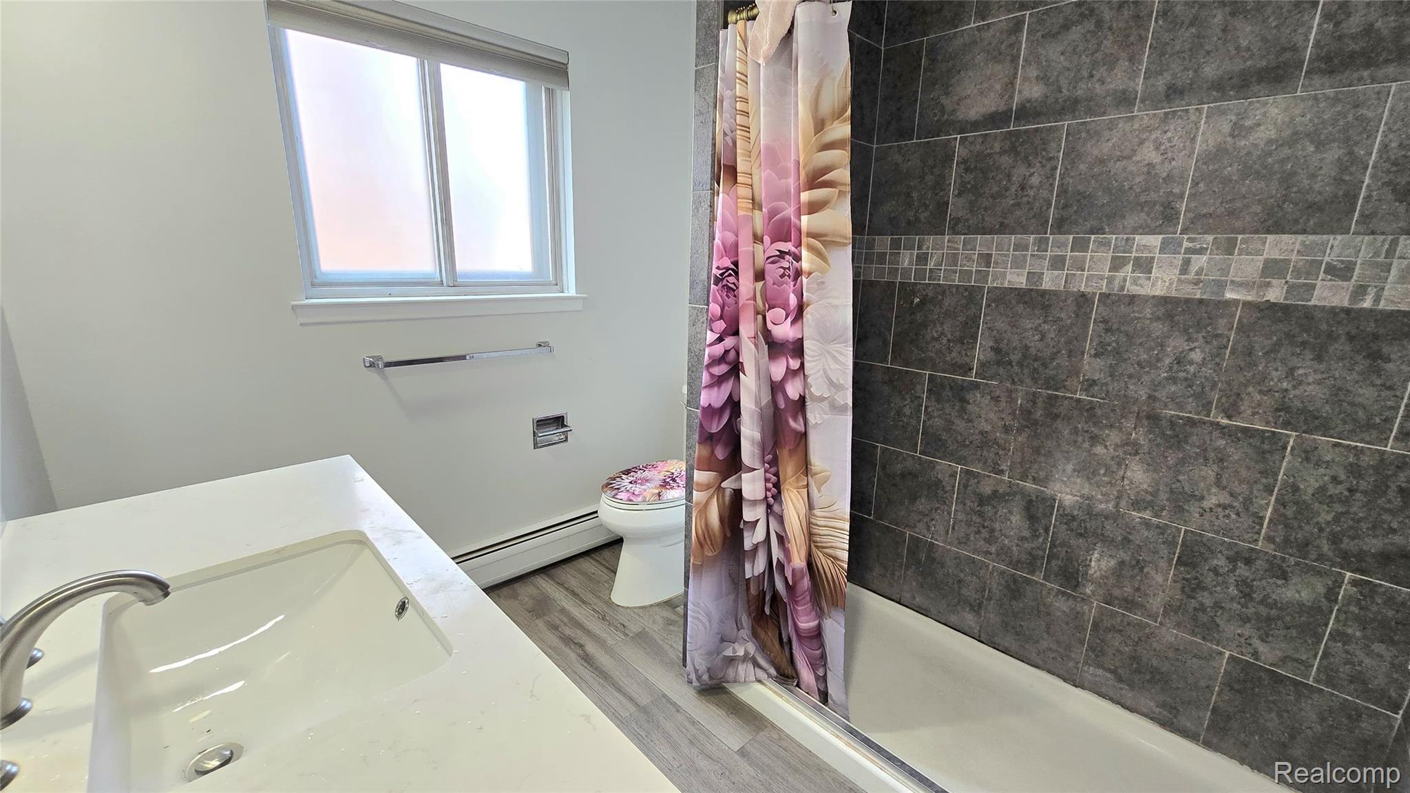 34294 Greentrees Road Sterling Heights, MI 48312 - Photo 11 of 20 Full bathroom featuring an integrated sink vanity, brushed nickel faucet, large format tile shower surround with mosaic accent, a built-in bathtub, and wood-finish flooring