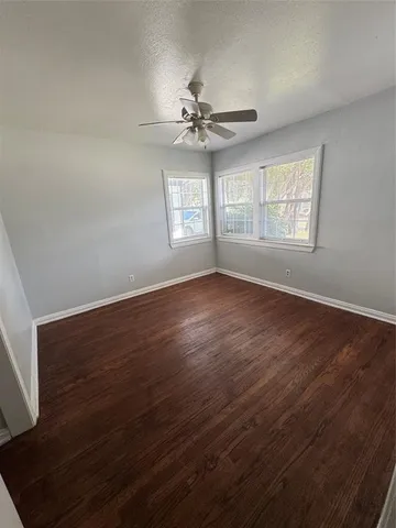 an empty room with wooden floor windows and fan