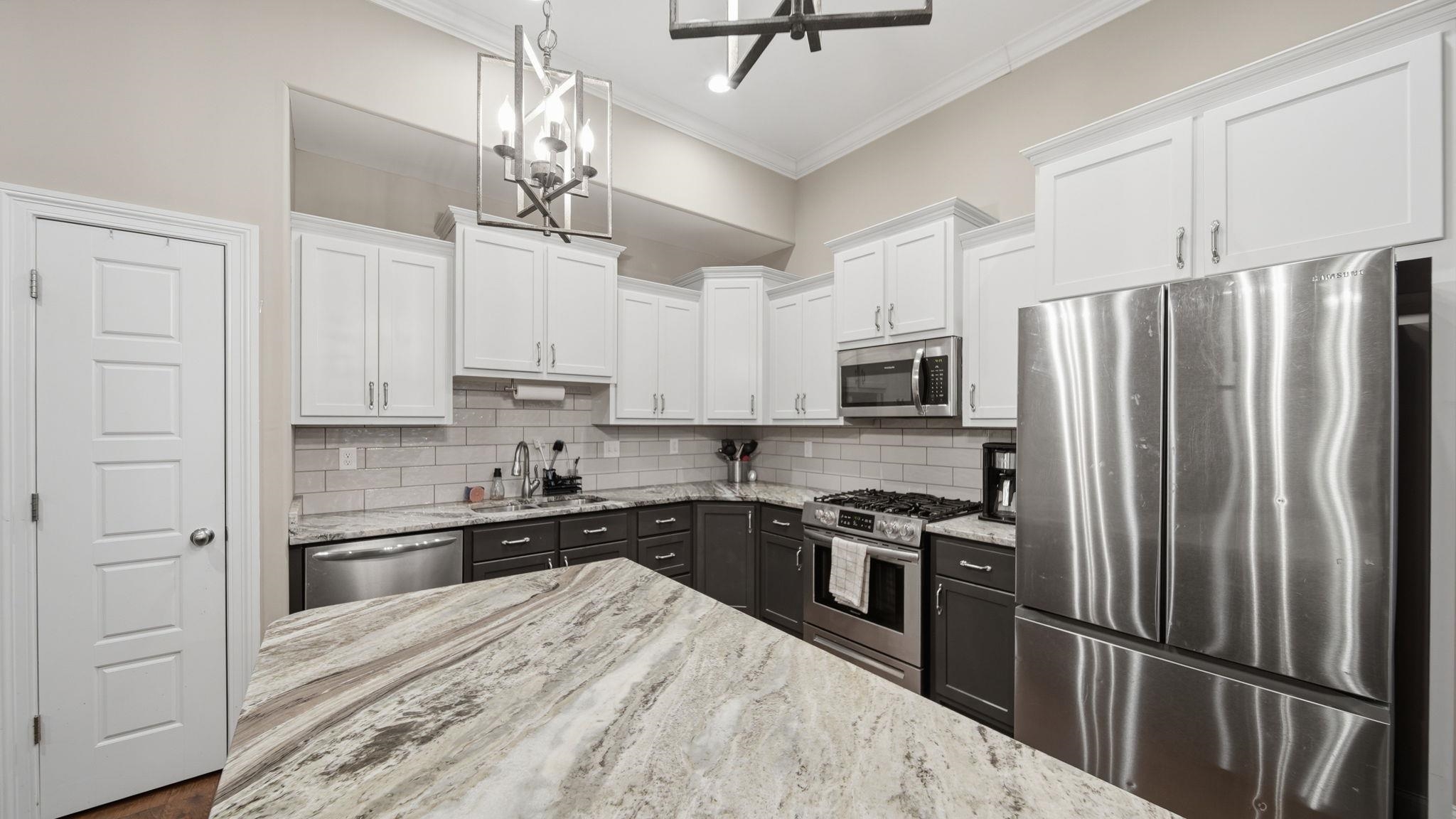 70 Trinity Cove Atoka, TN 38004 - Photo 7 of 25 Kitchen featuring a large central island with stone countertop, stainless steel appliances, white upper cabinetry, and dark lower cabinetry, complemented by a subway tile backsplash and vaulted ceiling