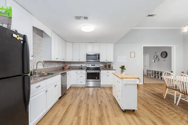 a kitchen with granite countertop a refrigerator a stove top oven a dining table and chairs with wooden floor