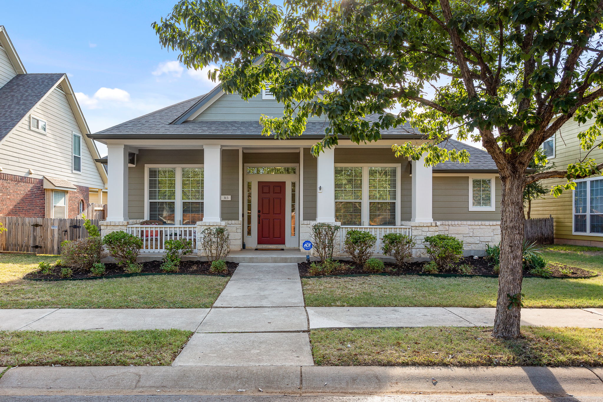 View of front facade with covered porch, roof with shingles, and stone siding