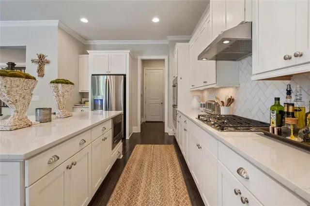 a open kitchen with stainless steel appliances kitchen island granite countertop a refrigerator a stove top oven a sink dishwasher and white cabinets with wooden floor