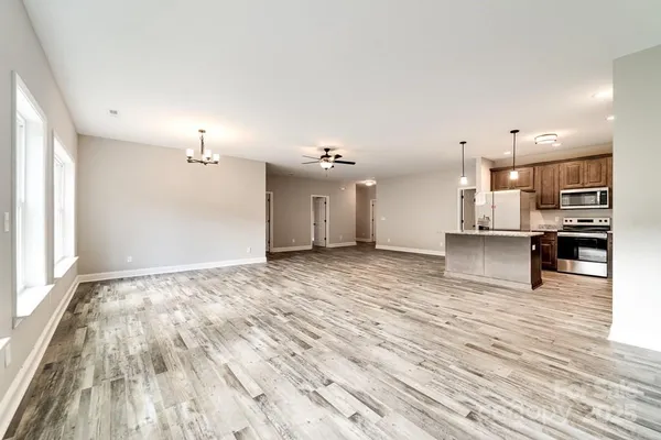 an empty room with wooden floor kitchen view and windows