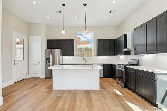 a kitchen with stainless steel appliances granite countertop a sink a stove a refrigerator and a wooden floor