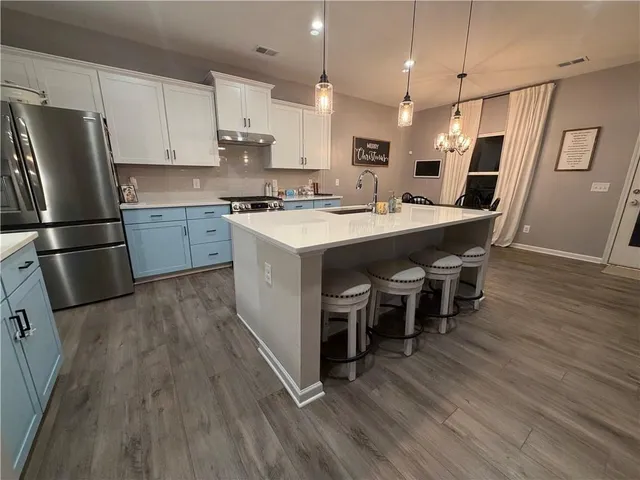 a kitchen with stainless steel appliances granite countertop a refrigerator a stove a sink dishwasher and a dining table with wooden floor