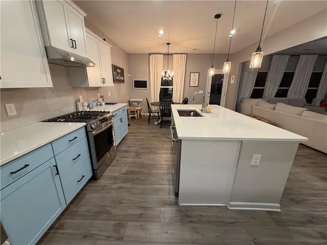 a large kitchen with stainless steel appliances kitchen island granite countertop a stove a sink a refrigerator and white cabinets with wooden floor