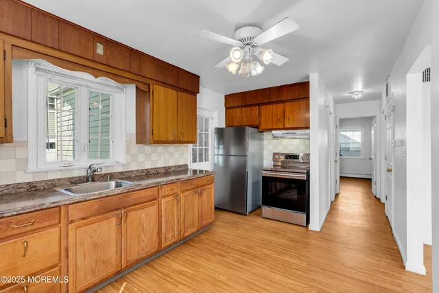 a kitchen with stainless steel appliances granite countertop a refrigerator a sink dishwasher a stove and white countertops with wooden floor