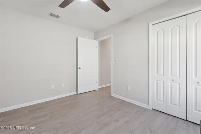 an empty room with wooden floor closet fan and windows
