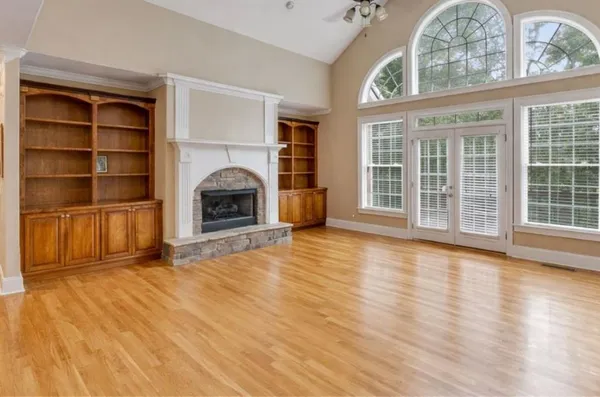 an empty room with wooden floor fireplace and windows