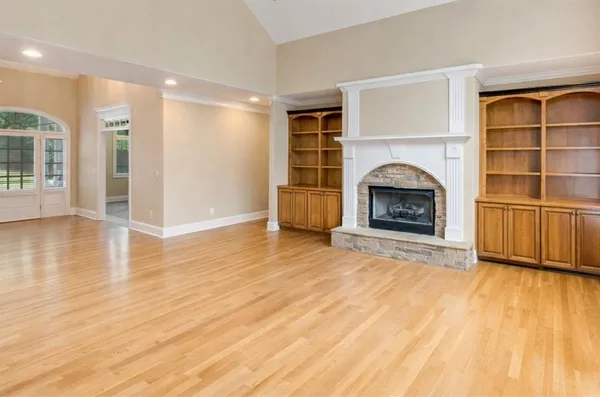 a view of an empty room with wooden floor fireplace and a window