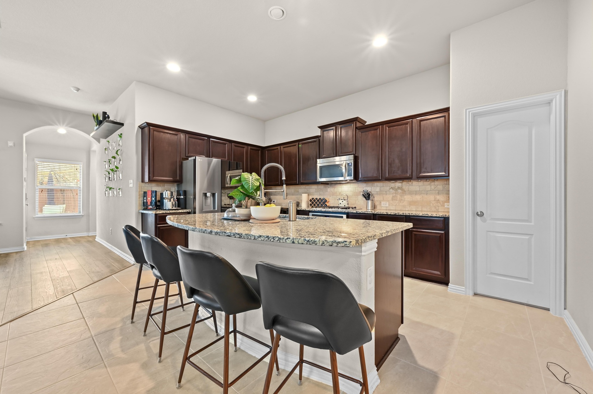 546 Hot Spring Valley Buda, TX 78610 - Photo 9 of 27 Kitchen with dark wood finish cabinetry, a breakfast bar, light stone counters, a kitchen island with sink, and backsplash