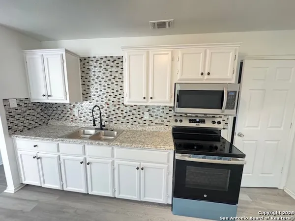 a kitchen with white cabinets a sink and a stove with wooden floor
