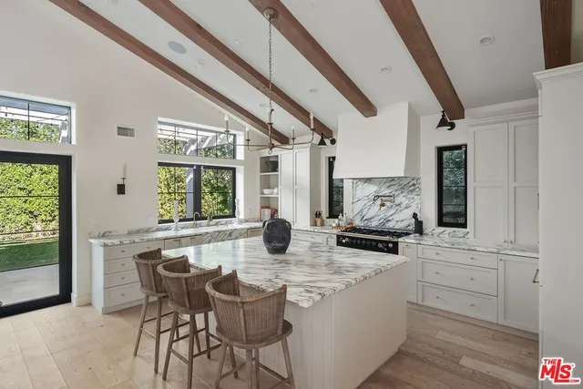 a kitchen with stainless steel appliances granite countertop a stove a sink and white cabinets with wooden floor next to windows