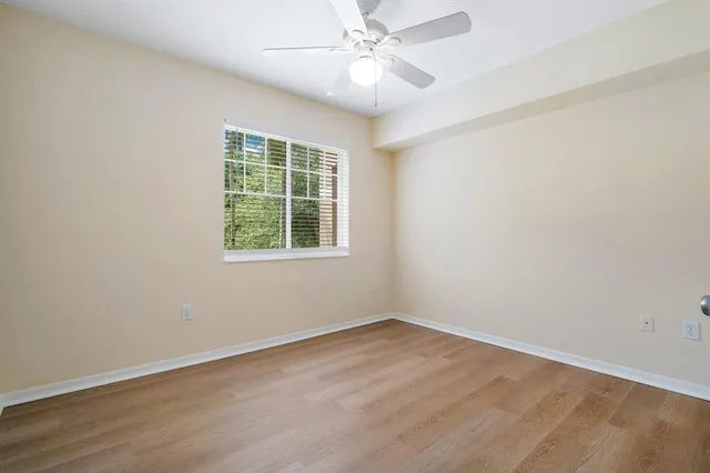 an empty room with wooden floor a ceiling fan and windows
