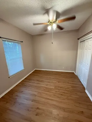 an empty room with wooden floor fan and windows