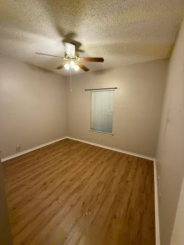 an empty room with wooden floor fan and windows