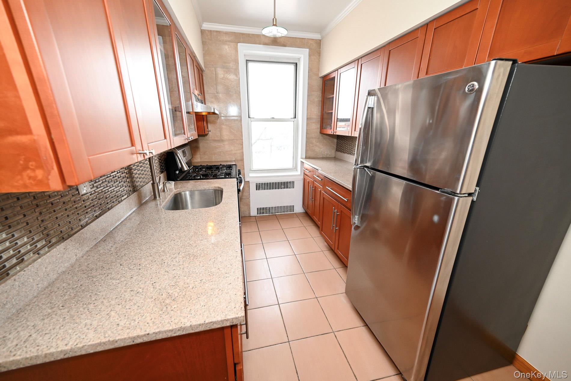 111-39 76th Road, Unit D7 Queens, NY 11375 - Photo 12 of 18 Kitchen featuring stainless steel appliances, radiator, brown cabinetry, and ornamental molding