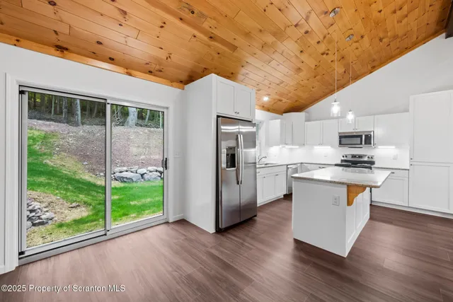 a kitchen with stainless steel appliances granite countertop a refrigerator a sink dishwasher a stove and a large window with wooden floor