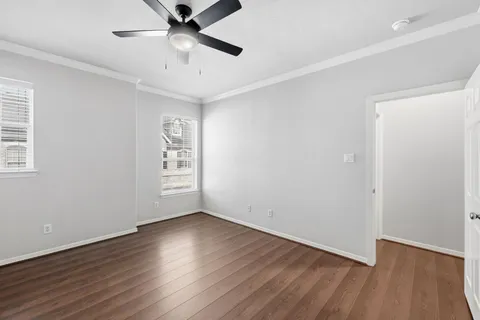 a view of an empty room with wooden floor and a ceiling fan