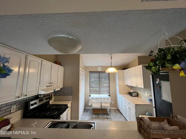 a kitchen with granite countertop a refrigerator a stove a sink and white cabinets