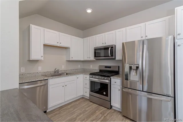 a kitchen with stainless steel appliances granite countertop a refrigerator stove a sink and dishwasher a refrigerator with wooden floor