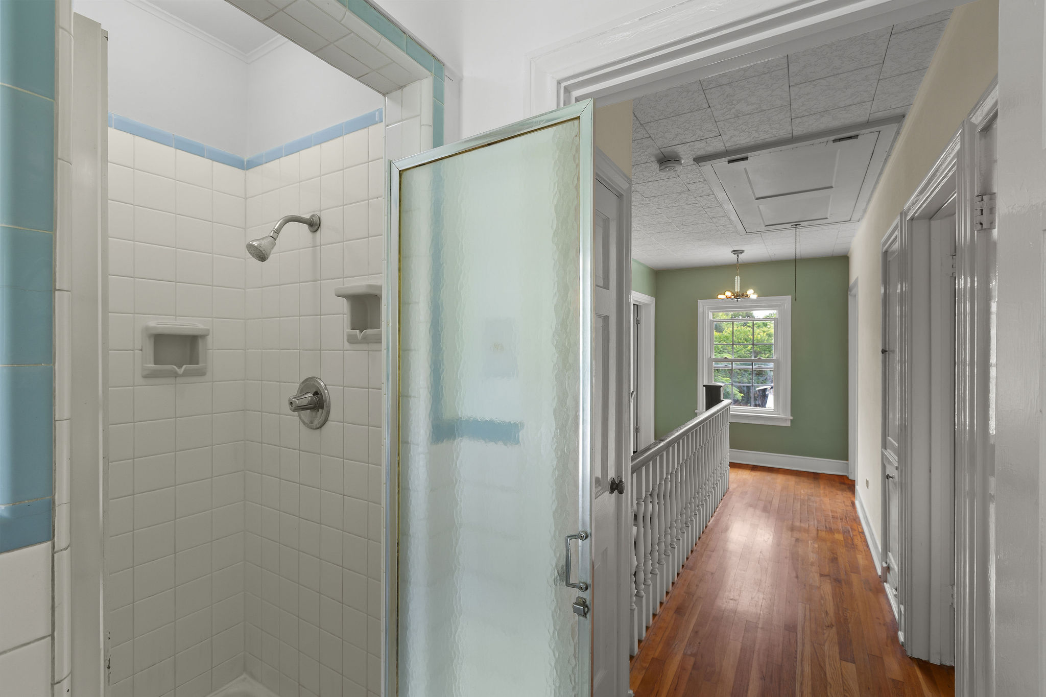 948 Maple Street Lockhart, TX 78644 - Photo 30 of 40 A classic tiled shower offers practical bathing, adjacent to a hallway with polished hardwood flooring.