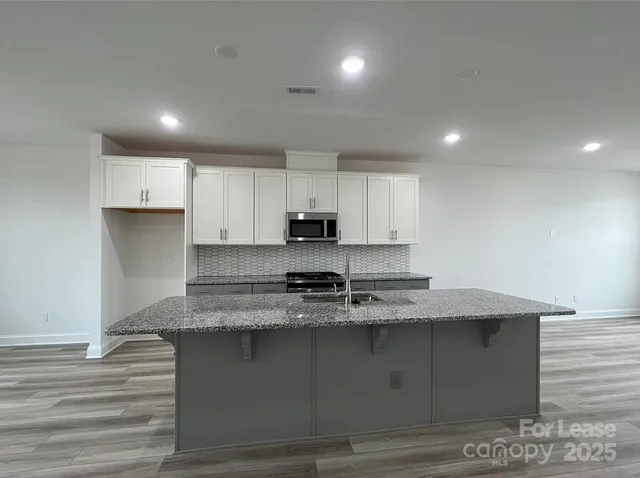 a kitchen with kitchen island granite countertop a sink a stove a oven and cabinets