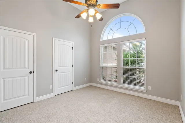 an empty room with chandelier fan and windows