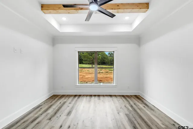 an empty room with wooden floor windows and fan
