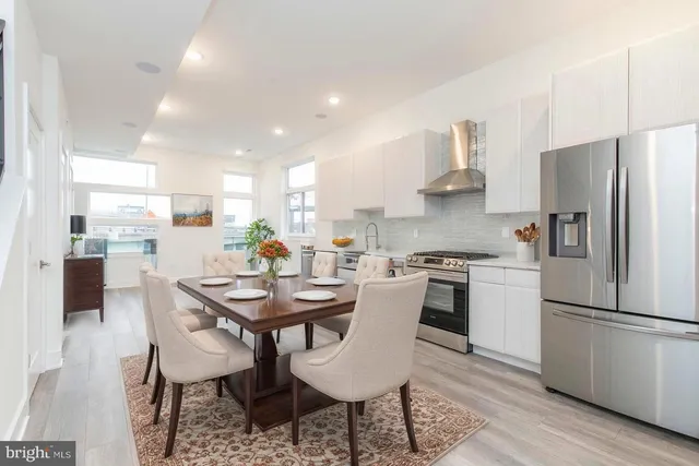 a kitchen with stainless steel appliances kitchen island granite countertop a dining table chairs and a refrigerator
