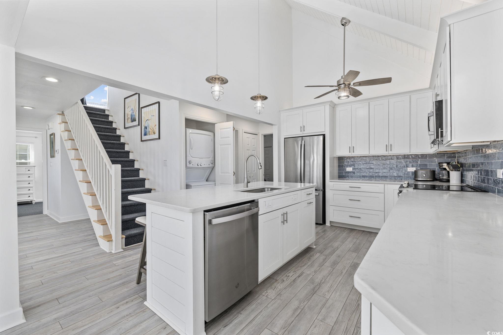 27 Riptide Lane Pawleys Island, SC 29585 - Photo 12 of 40 Kitchen featuring high vaulted ceiling, white cabinets, hanging light fixtures, appliances with stainless steel finishes, and an island with sink
