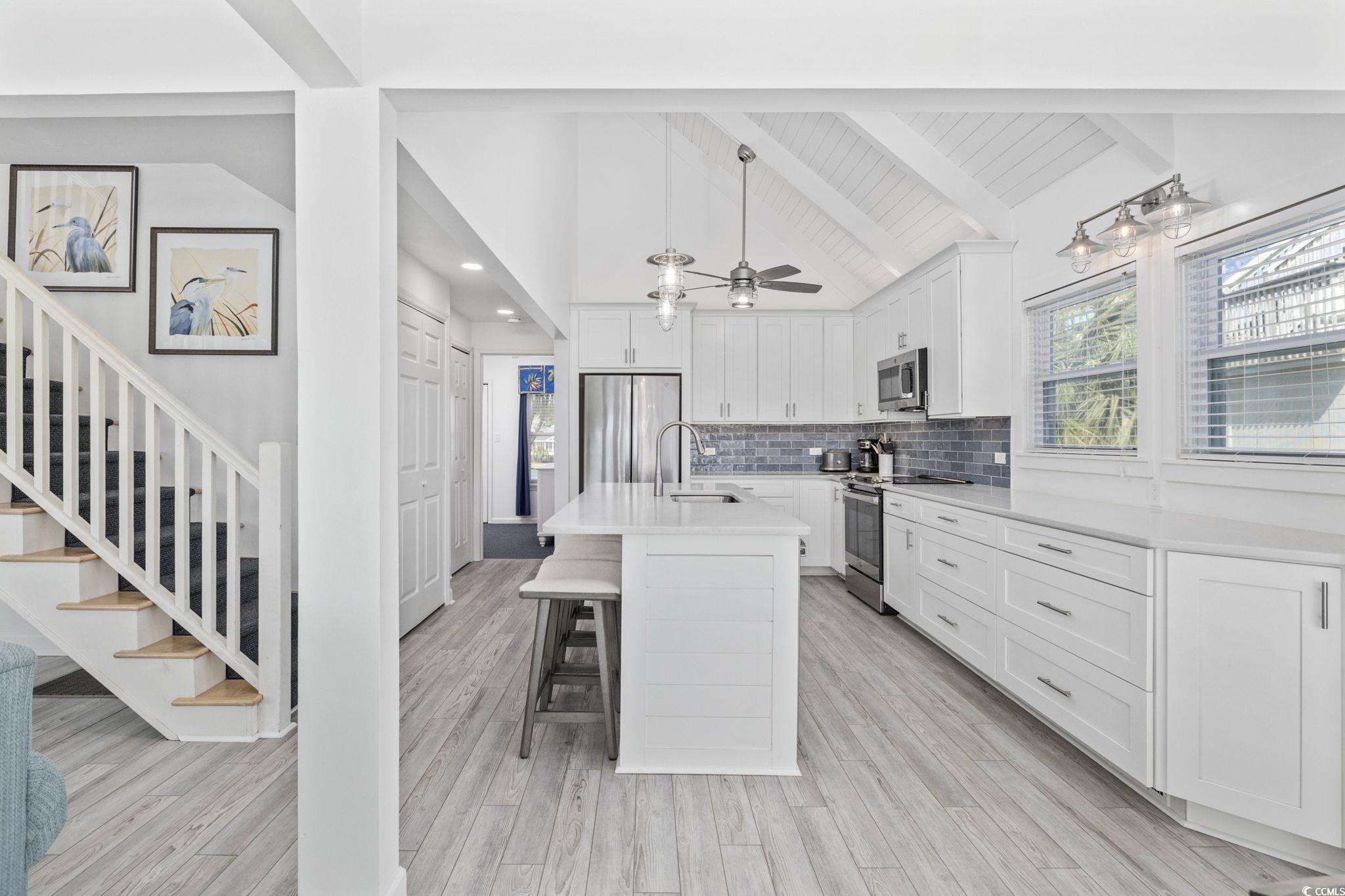 27 Riptide Lane Pawleys Island, SC 29585 - Photo 13 of 40 Kitchen with white cabinetry, stainless steel appliances, backsplash, a kitchen breakfast bar, and an island with sink