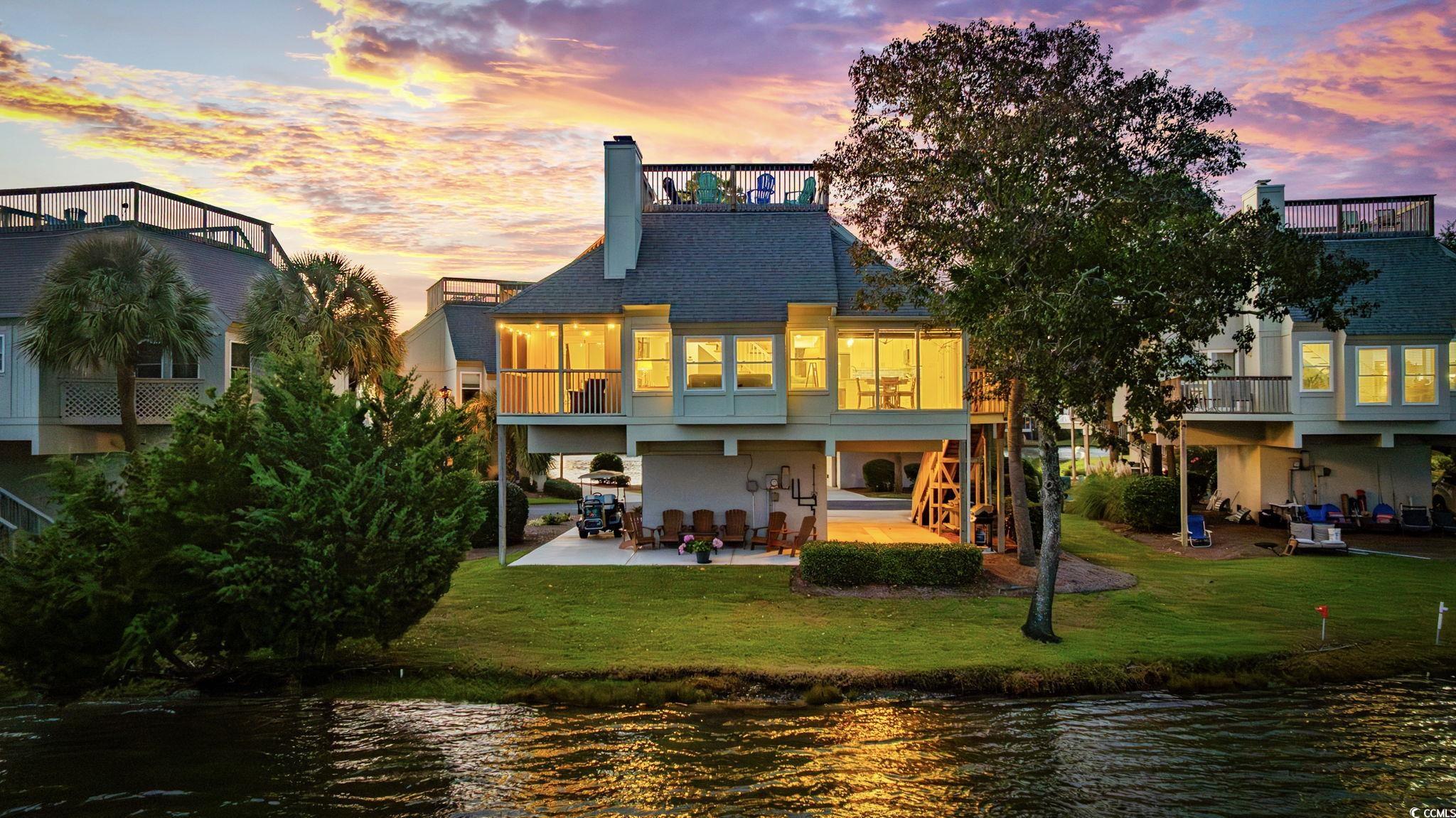 27 Riptide Lane Pawleys Island, SC 29585 - Photo 2 of 40 Rear view of house featuring a patio area, a water view, a chimney, and a lawn