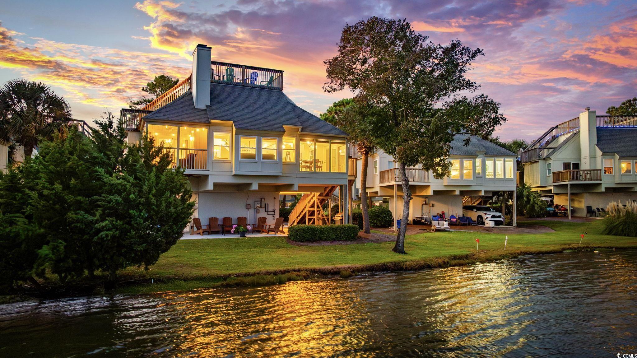27 Riptide Lane Pawleys Island, SC 29585 - Photo 30 of 40 Back of property at dusk featuring a water view, a patio area, a yard, and a chimney