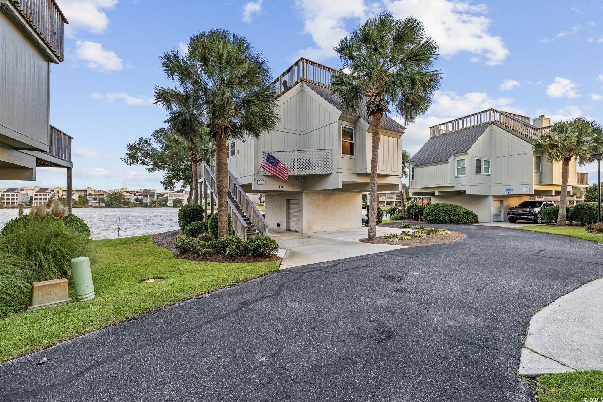 27 Riptide Lane Pawleys Island, SC 29585 - Photo 4 of 40 View of front of property with stairway, a water view, a front lawn, a carport, and a balcony