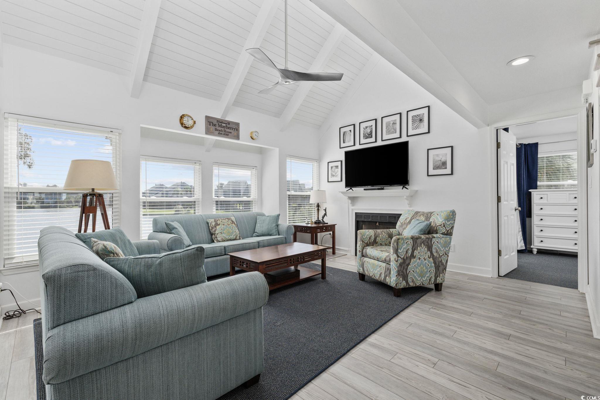 27 Riptide Lane Pawleys Island, SC 29585 - Photo 7 of 40 Living room featuring beamed ceiling, ceiling fan, a fireplace, healthy amount of natural light, and light wood-style floors