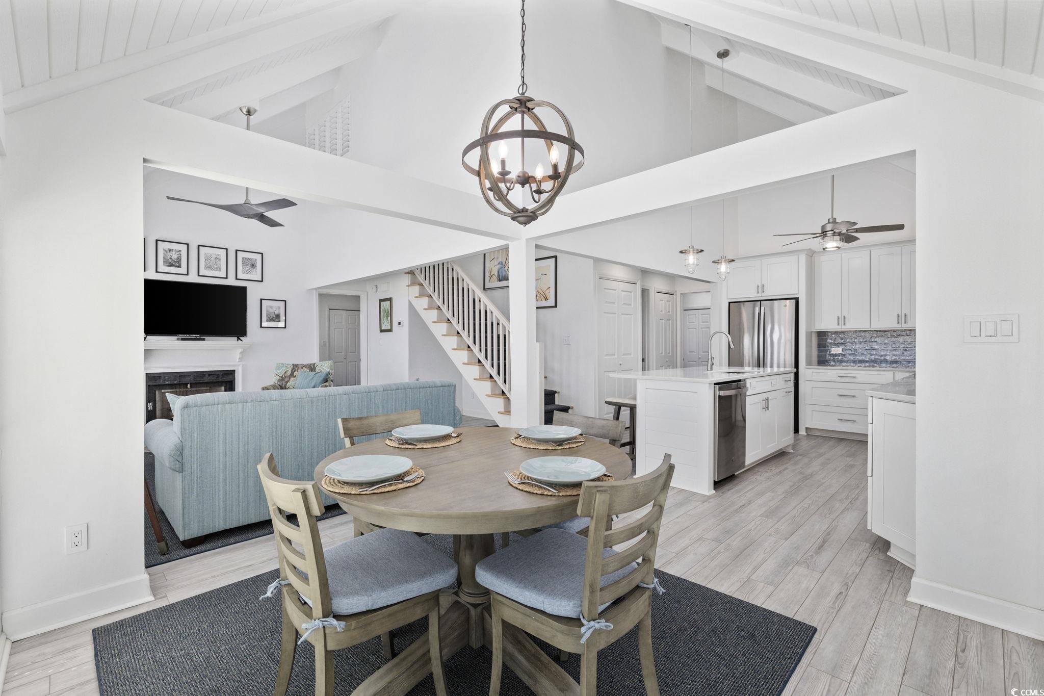27 Riptide Lane Pawleys Island, SC 29585 - Photo 10 of 40 Dining area featuring ceiling fan, stairway, a fireplace, light wood-style floors, and beam ceiling